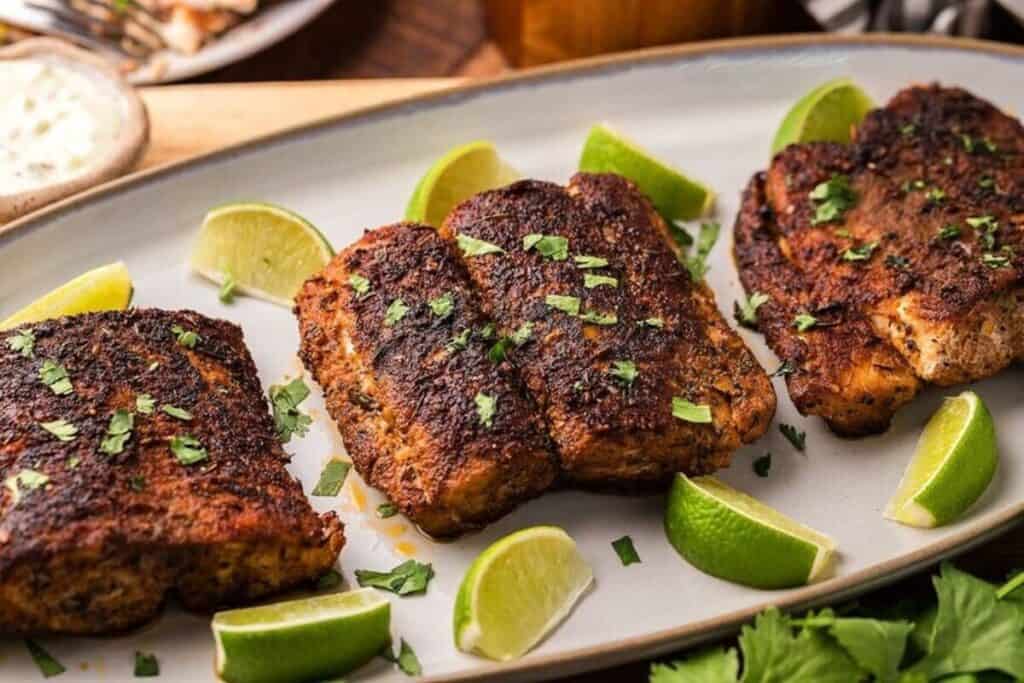 Three pieces of blackened fish are arranged on a platter with lime wedges and sprinkled with chopped herbs&mdash;a flavorful choice for easy weeknight dinners.