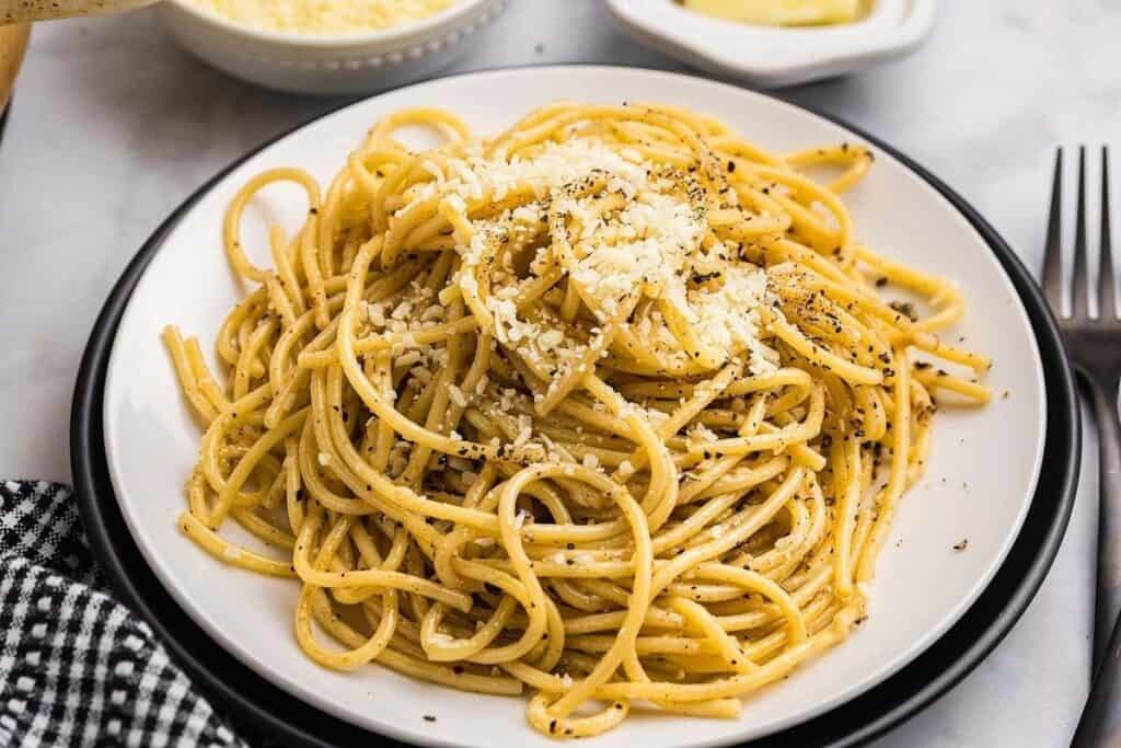 A plate of Pasta Classics spaghetti topped with grated cheese and black pepper, set on a white plate with a fork beside it.