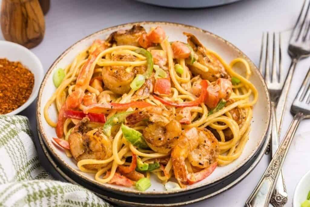 A plate of Pasta Classics featuring shrimp, bell peppers, and green onions, garnished with spices, set on a table with a fork and knife beside it.