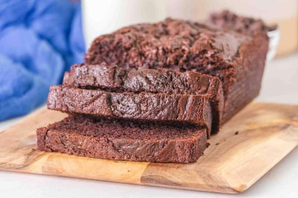 A loaf of chocolate bread with several slices cut, displayed on a wooden cutting board.