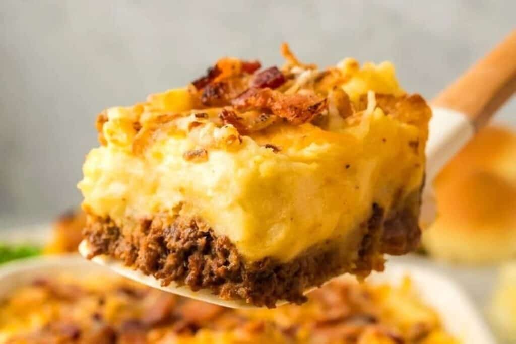 A close-up of a spatula lifting a slice of casserole with a ground meat base, mashed potato topping, melted cheese, and bacon bits&mdash;perfect inspiration for hearty Casserole Recipes.