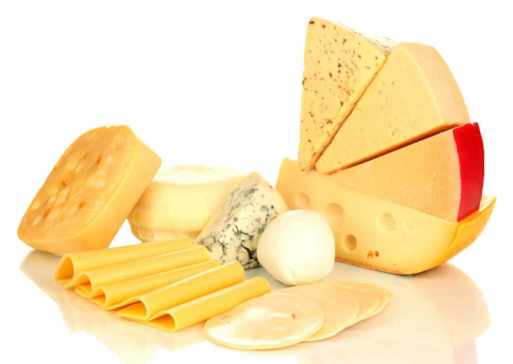 An assortment of cheeses including slices, wedges, and rounds of various types such as gouda, blue cheese, mozzarella, and Swiss, arranged together on a white surface.