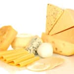 An assortment of cheeses including slices, wedges, and rounds of various types such as gouda, blue cheese, mozzarella, and Swiss, arranged together on a white surface.