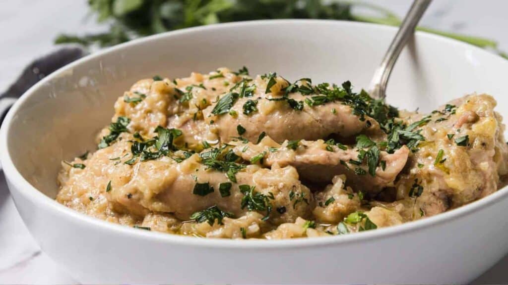 Chicken in a creamy sauce garnished with chopped herbs, served in a white bowl with a spoon.