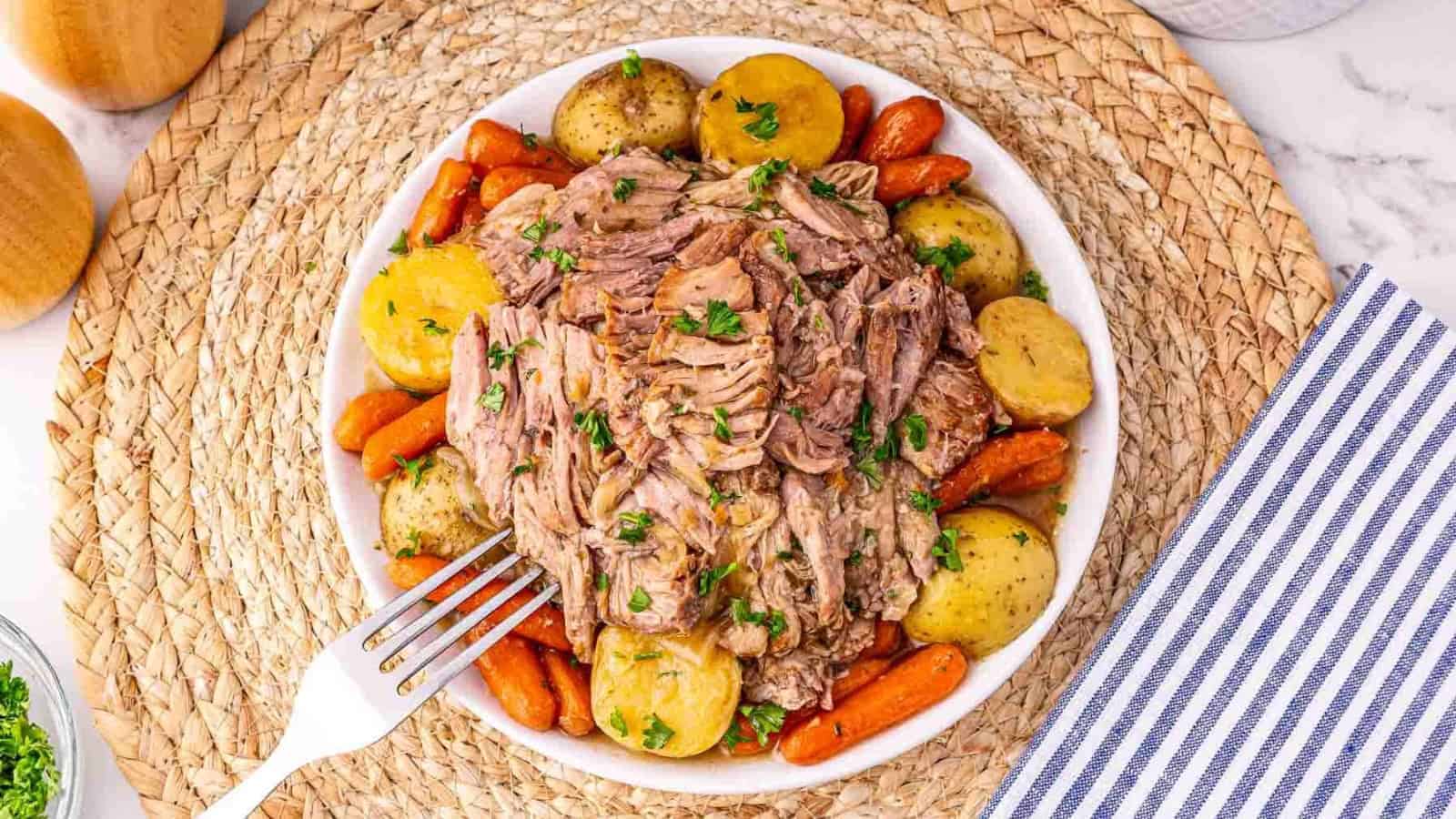 A bowl of shredded pot roast with baby potatoes and carrots, garnished with parsley, on a woven placemat.