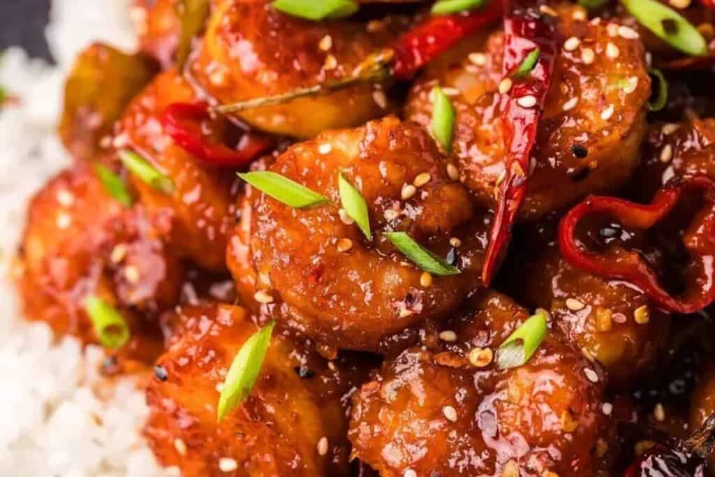 Close-up of spicy shrimp glazed in a red sauce, garnished with sliced green onions, sesame seeds, and dried red chilies, served over white rice&mdash;perfect for easy Weeknight Dinners.