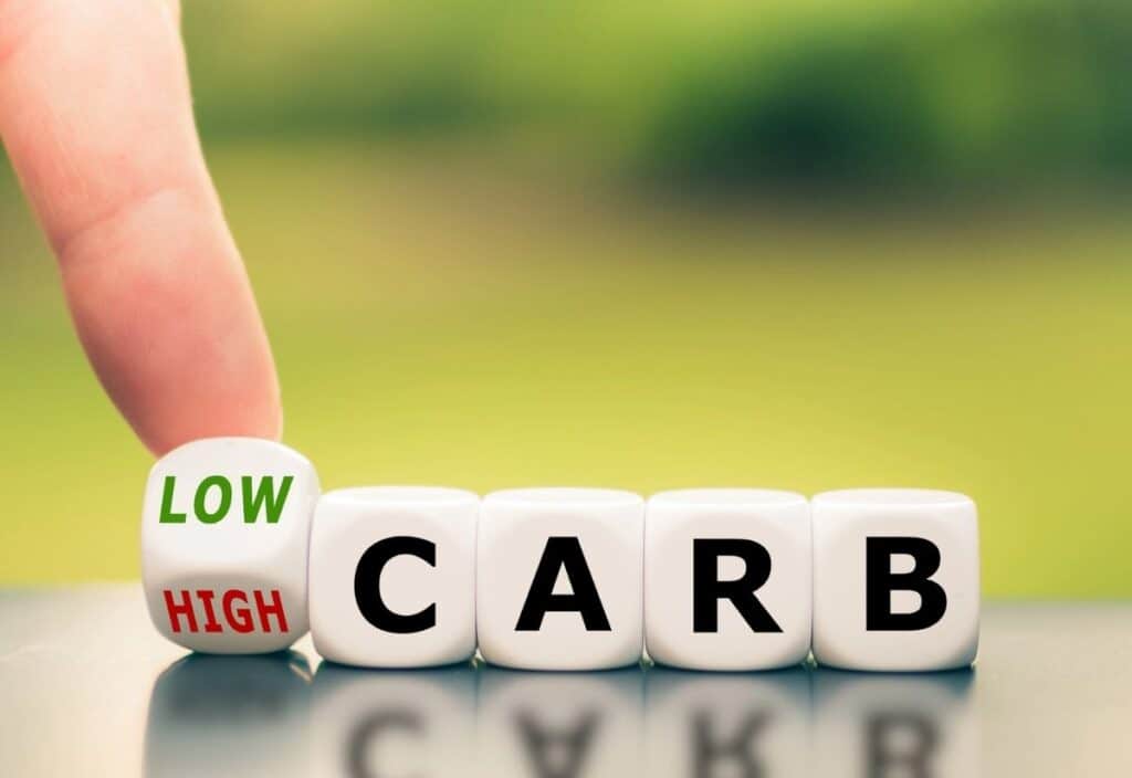 A hand flips a die showing "LOW" and "HIGH" beside blocks spelling "CARB," symbolizing carb choices&mdash;perfect for celebrating National Keto Day.