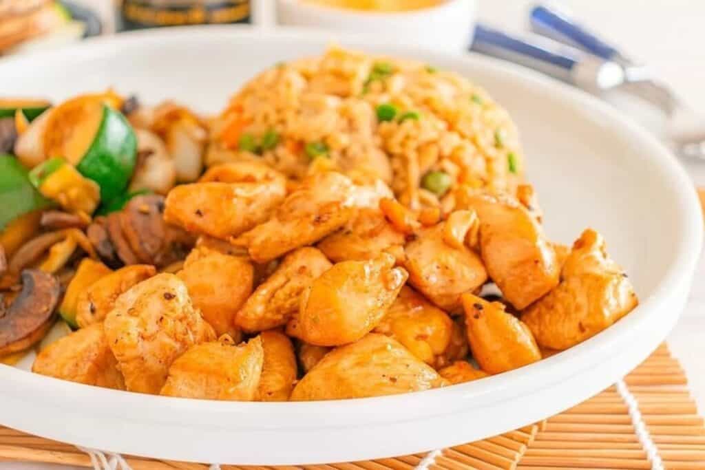 A white plate with grilled chicken pieces, saut&eacute;ed vegetables like zucchini and mushrooms, and a serving of fried rice with peas&mdash;perfect for easy Weeknight Dinners.