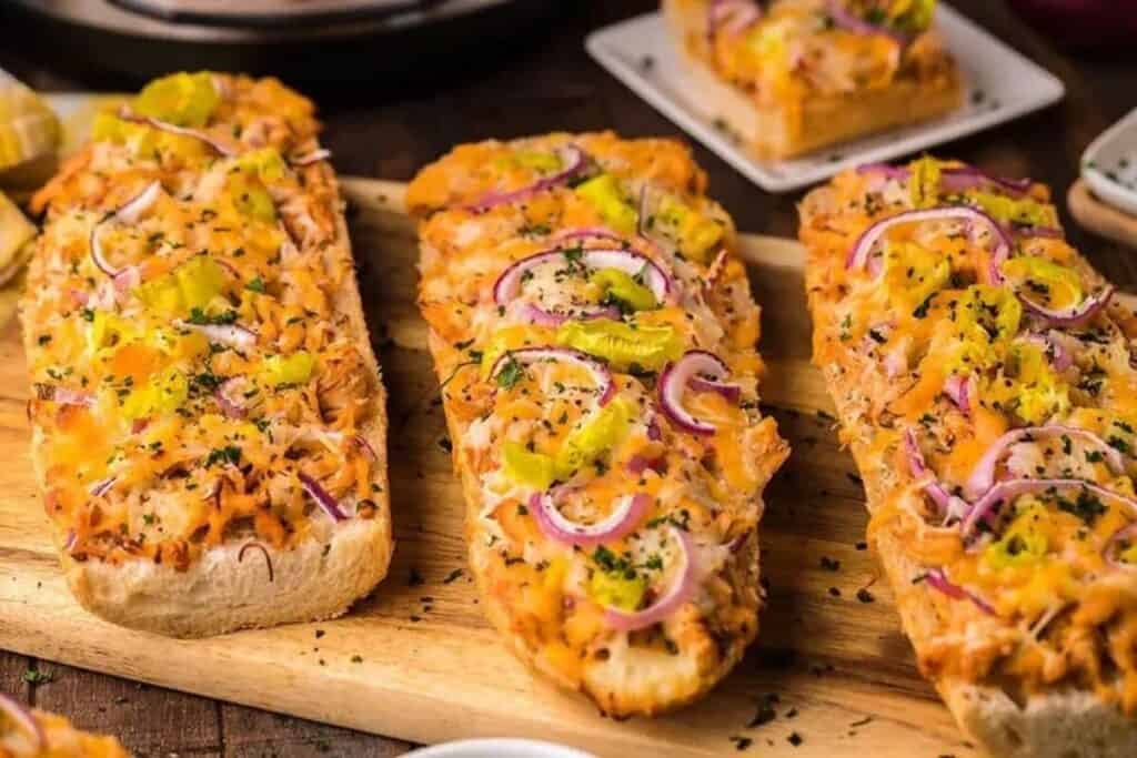 Three pieces of cheesy bread topped with shredded cheese, red onion slices, and yellow peppers are arranged on a wooden board&mdash;perfect for easy weeknight dinners.
