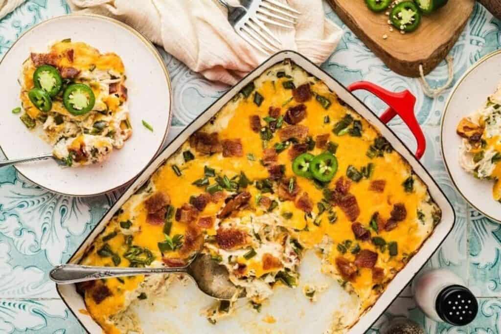 A casserole dish filled with a baked cheesy casserole, topped with bacon and jalape&ntilde;o slices, with a portion served on a plate nearby&mdash;perfect inspiration for your next Casserole Recipes adventure.