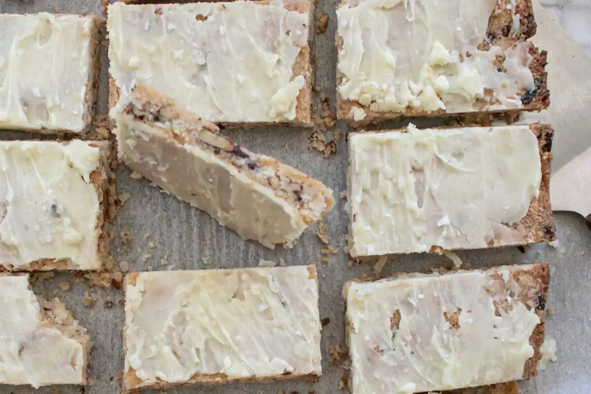 Rectangular bars with a pale, creamy frosting are arranged on parchment paper; one bar is tilted on its side among the others.