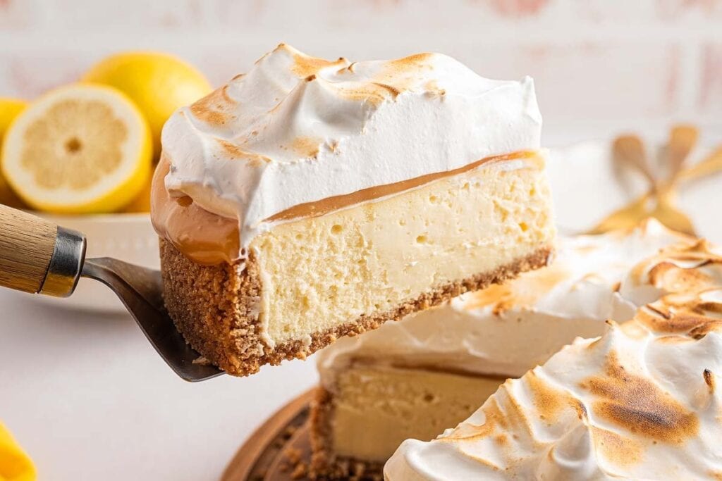 A slice of lemon meringue cheesecake with a graham cracker crust is lifted from the whole cake, its toasted meringue topping making it one of the easiest desserts to impress any crowd.