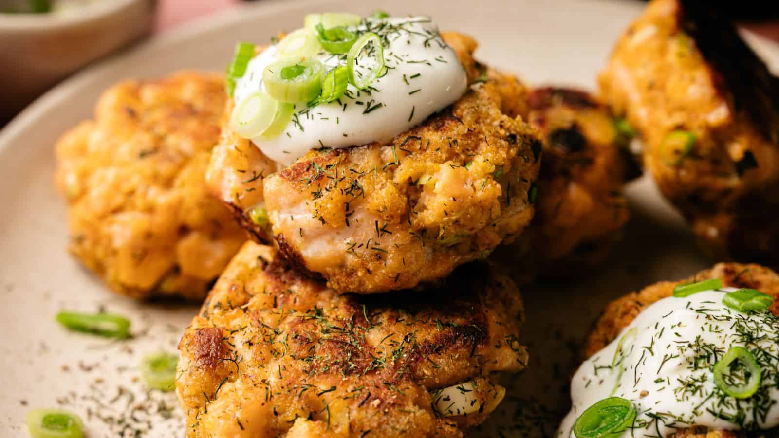 A plate of salmon patties topped with a dollop of sour cream, chopped green onions, and sprinkled with herbs.