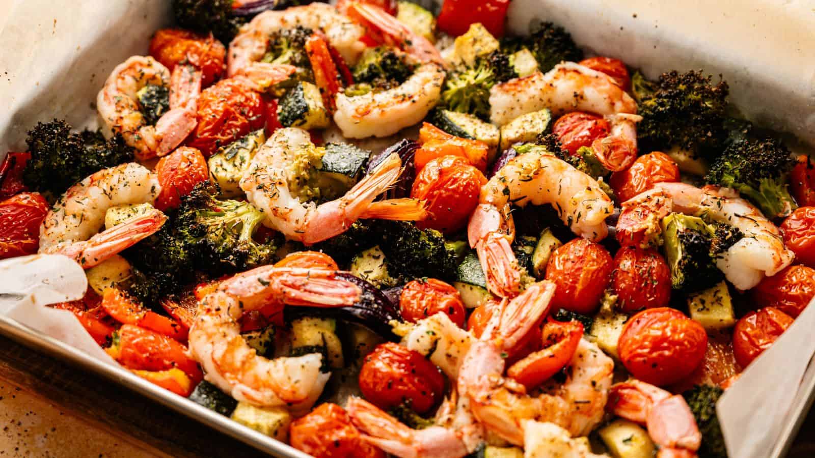 Sheet pan of roasted shrimp, cherry tomatoes, broccoli, and zucchini, seasoned with herbs and baked on parchment paper.