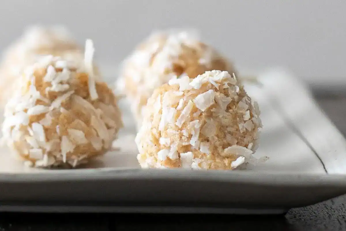 Close-up of coconut-covered dessert balls arranged on a rectangular white plate.