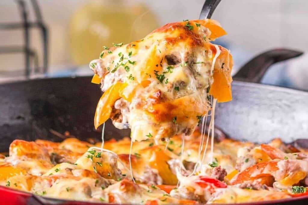 A close-up of a cheesy casserole being served from a skillet, showing melted cheese, ground meat, and sliced bell peppers&mdash;an irresistible choice for those who love comforting Casserole Recipes.