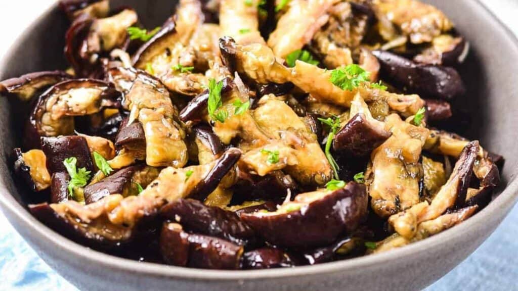 A bowl of cooked eggplant strips garnished with chopped parsley.