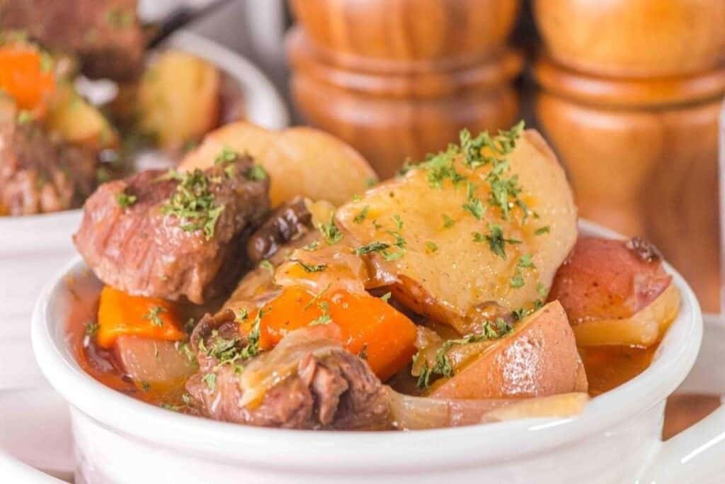 A bowl of beef stew with chunks of beef, potatoes, carrots, onions, and parsley garnish&mdash;perfect for those who love hearty slow cooked meals.