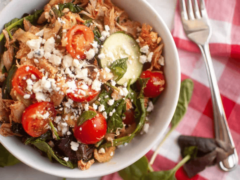 A bowl of Buffalo Chicken Salad on a white table with a red checkered napkin and a fork beside it.