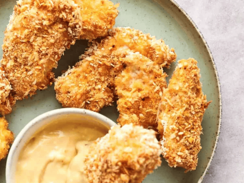 Breaded chicken tenders served on a plate with dipping sauce.