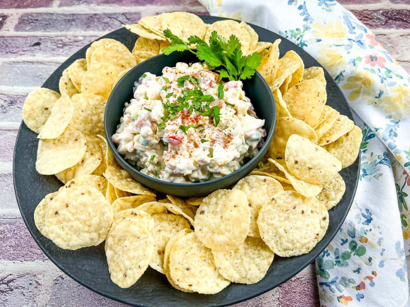 A bowl of Chilled Corn Dip with chips on a black plate.