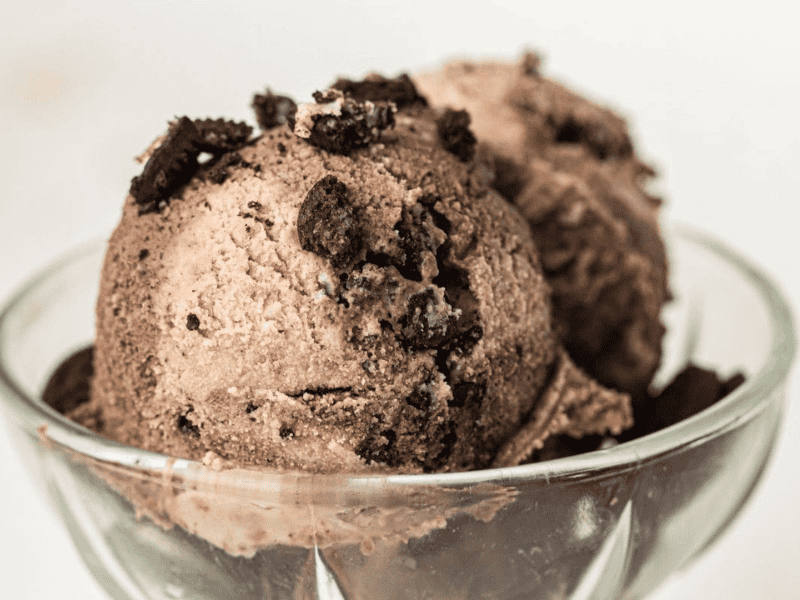 Two scoops of chocolate ice cream with crushed cookies on top, served in a clear glass bowl.