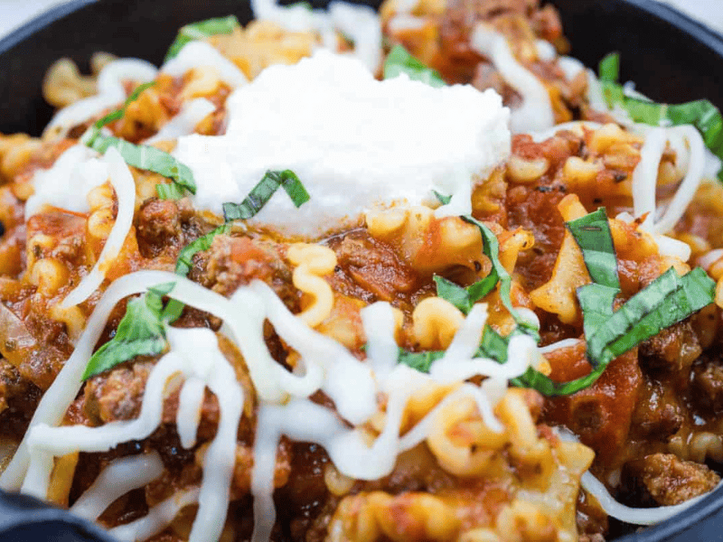 A skillet lasagna topped with melted cheese, a dollop of ricotta, and fresh basil.