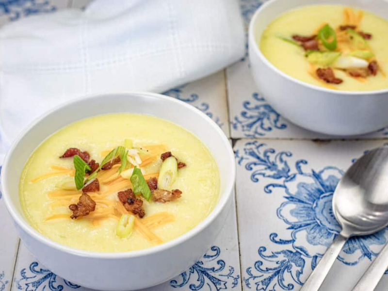 Two bowls of Copycat La Madeleine Country Potato Soup were placed on a marble surface next to two spoons.