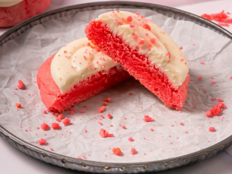 A Crumbl Copycat Pink Velvet Cookies is cut in half and displayed on a round metal tray lined with crinkled parchment paper.