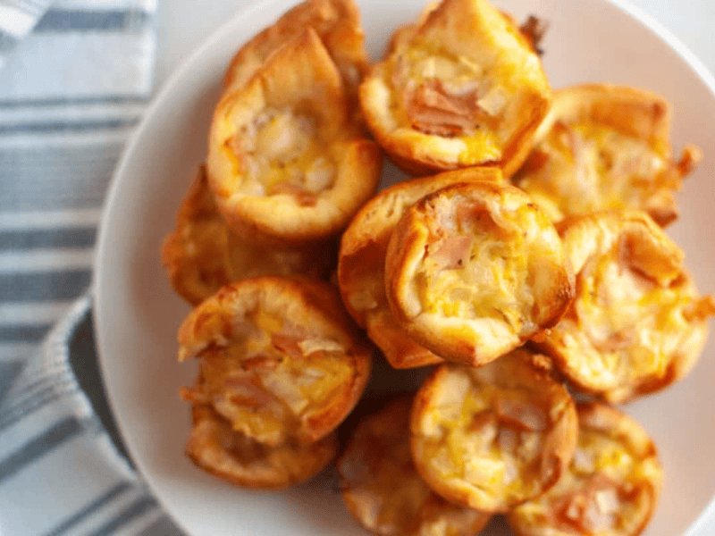 Overhead close-up of a white plate filled with small, golden-brown Ham & Cheese Puffs.