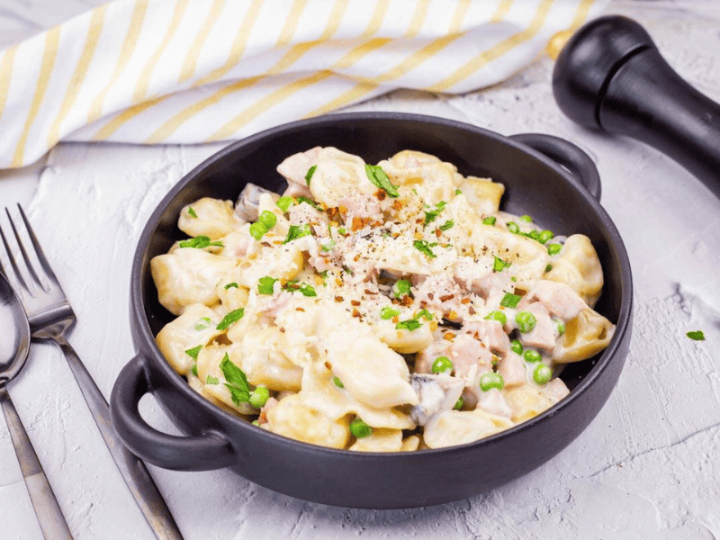 A black bowl of Easy Skillet Cheese Tortellini with Ham & Peas garnished with grated cheese and herbs.