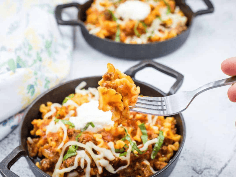 Two cast-iron skillets filled with skillet lasagna, topped with melted cheese.