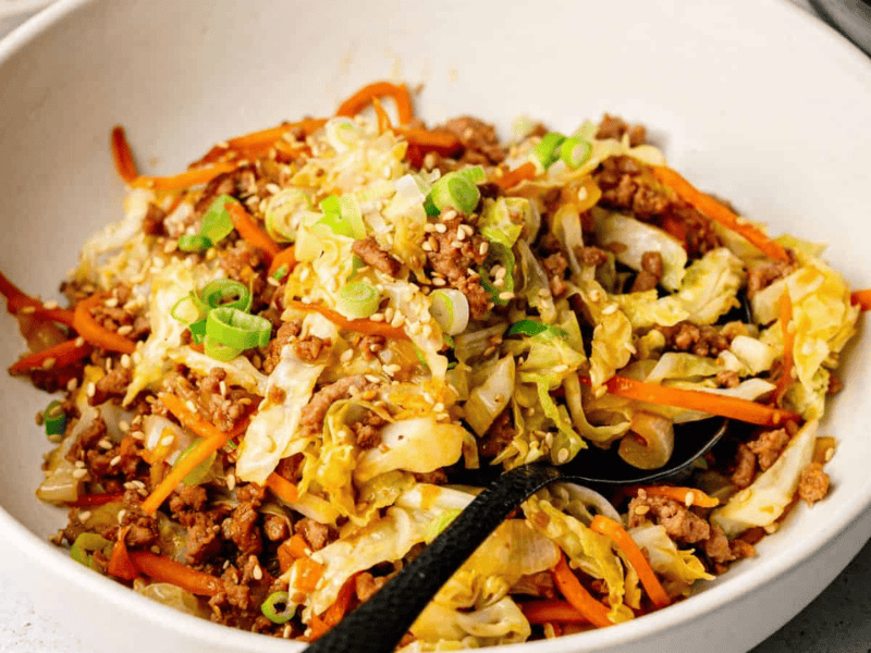A bowl of stir-fried ground meat, shredded cabbage, and carrots, topped with sesame seeds and chopped green onions.