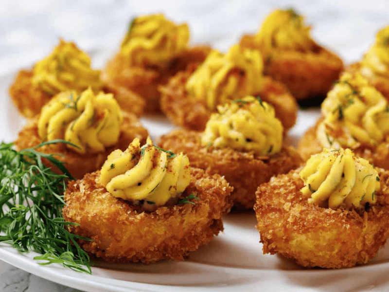A close-up shot of fried deviled eggs on a white plate, with a focus on the texture and garnish.