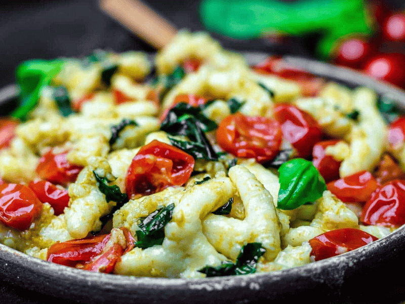Brown plate with gnocci, tomatoes and basil leaves.