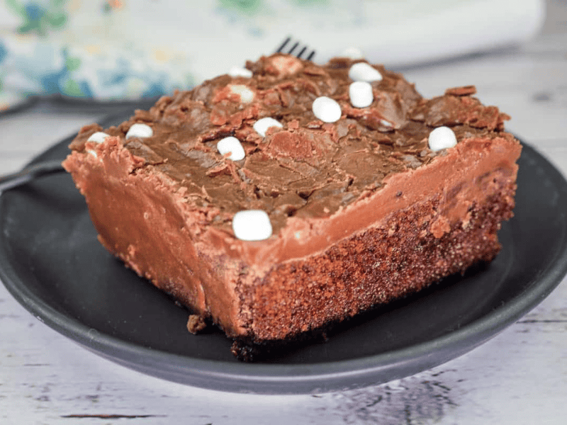 A slice of Grandma's Coca-Cola cake with chocolate frosting and small marshmallows on a black plate.