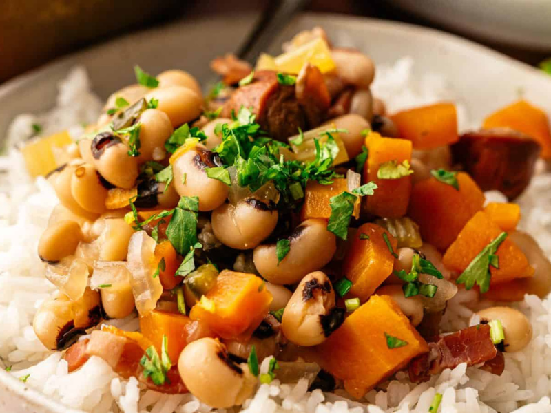 A bowl of white rice topped with black-eyed peas, diced sweet potatoes, onions, herbs, and chopped parsley.