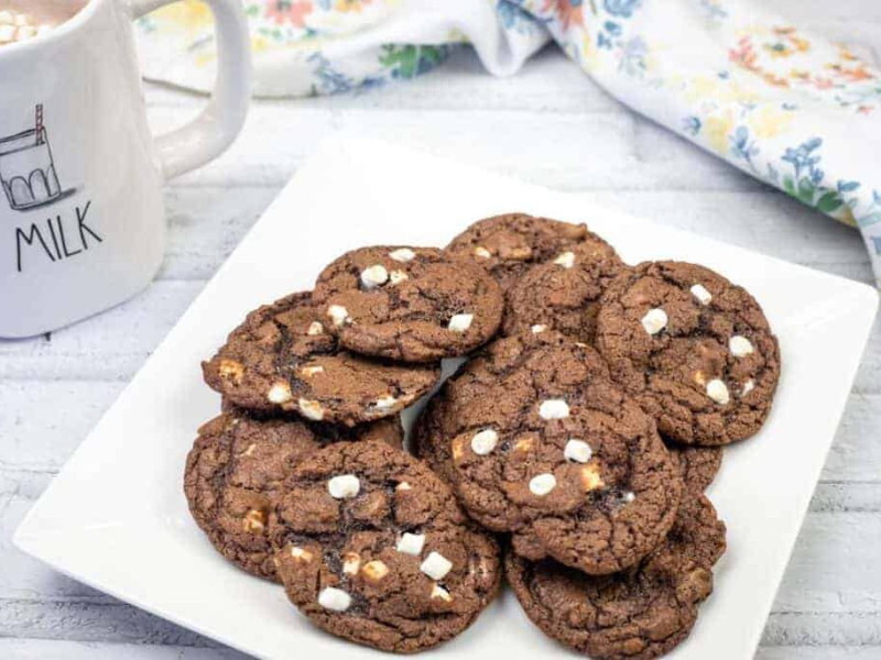 A white square plate with a stack of chocolate cookies featuring white chocolate chips.