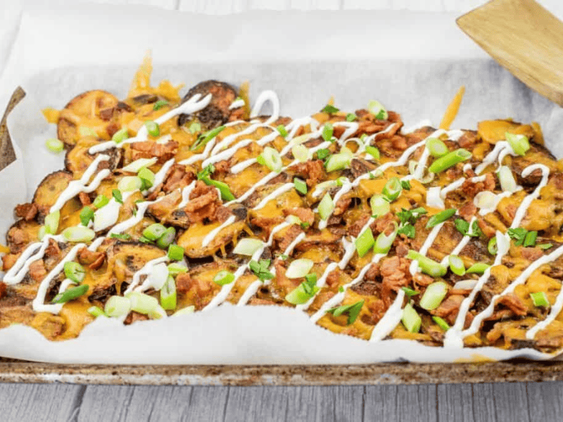 Tray of Irish nachos topped with green onions, bacon, cheese, and drizzled with sour cream.