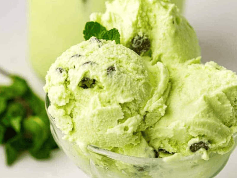 Three scoops of mint chocolate chip ice cream in a glass bowl, garnished with a sprig of mint.
