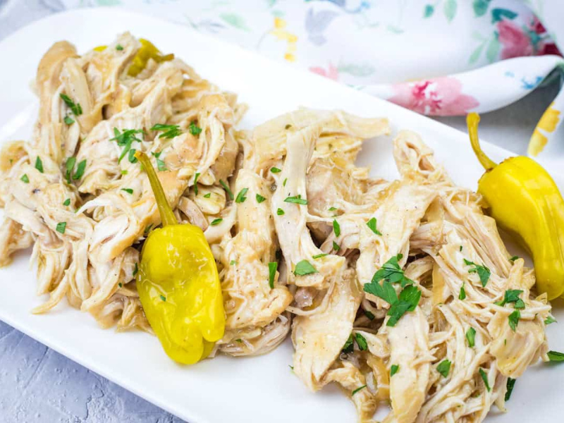 Mississippi Chicken - Slow Cooker with herbs and two yellow peppers on a white rectangular plate.