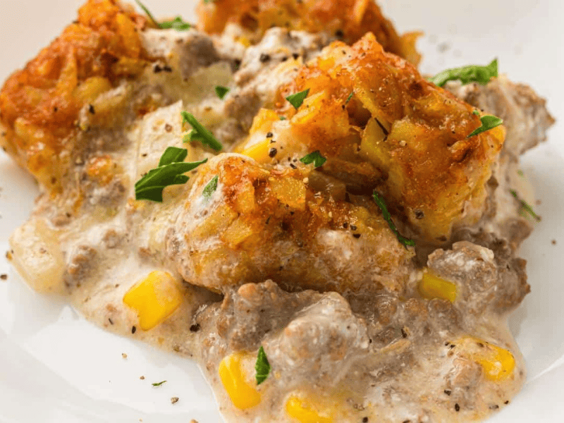 A serving of Slow Cooker Cowboy Casserole topped with crispy tater tots and black pepper on a white plate.