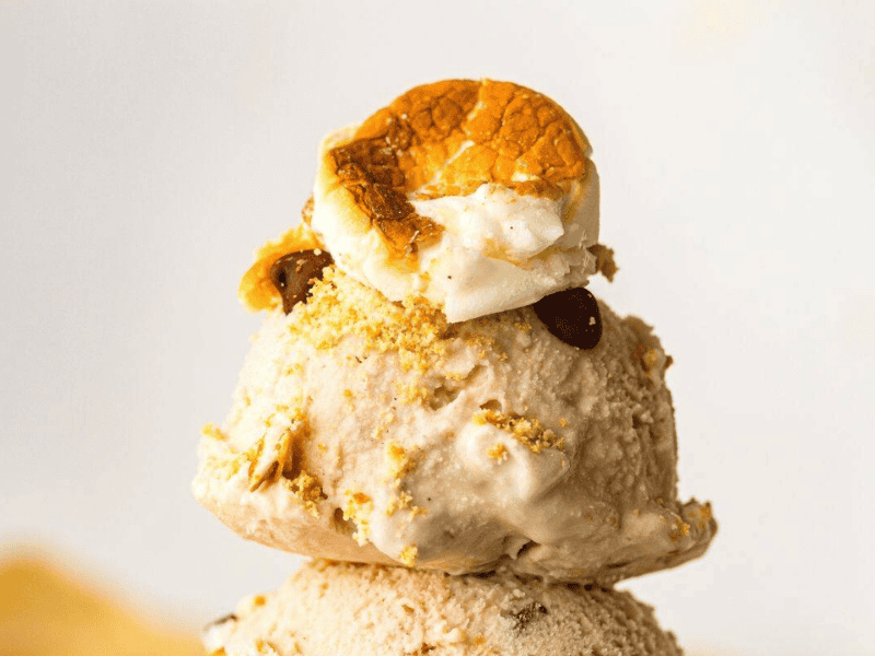 A scoop of S’mores ice cream topped with crushed graham crackers, chocolate chips, and a toasted marshmallow.