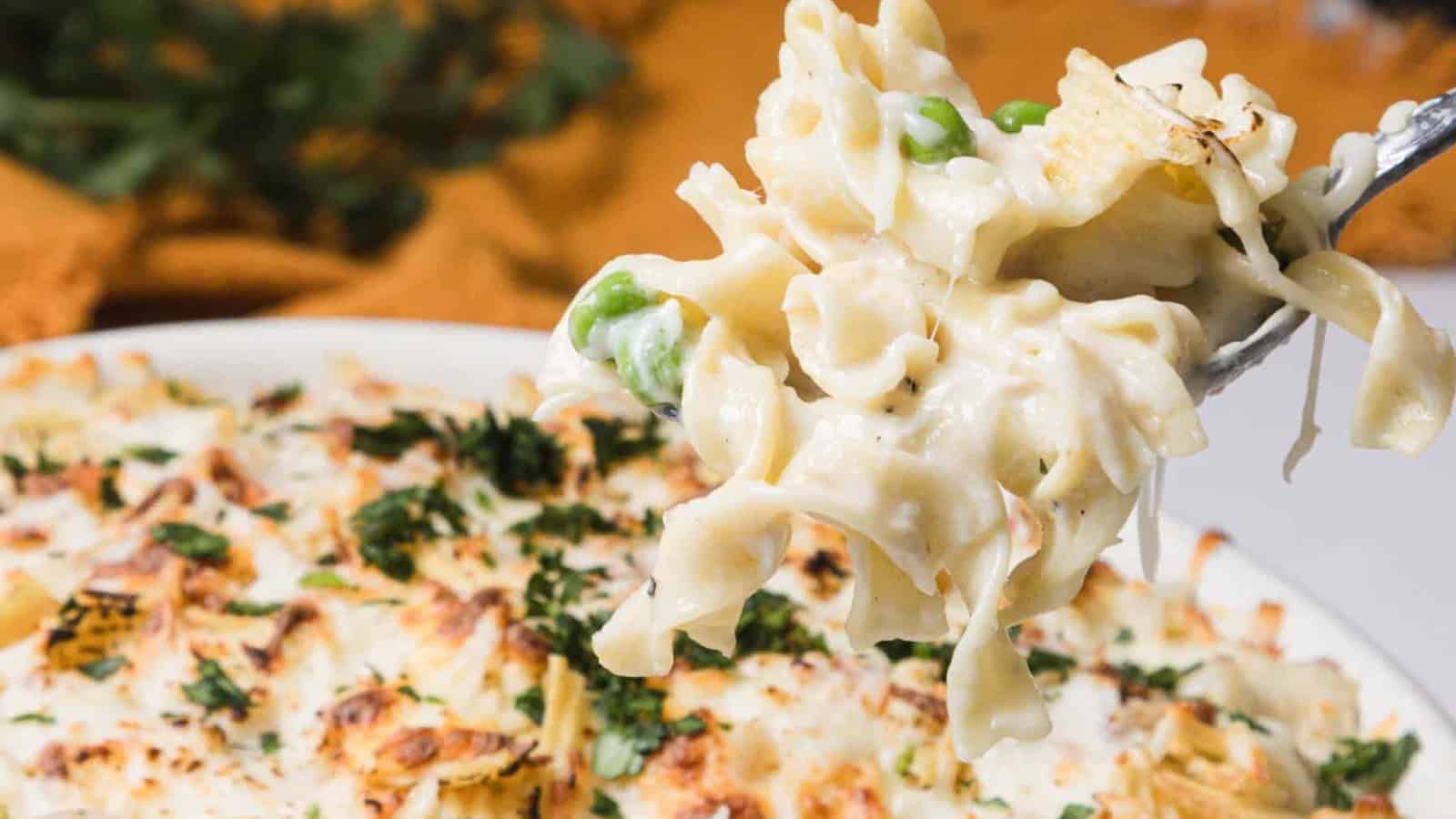 A fork lifts creamy pasta bake with peas and cheese from a casserole dish, garnished with herbs.