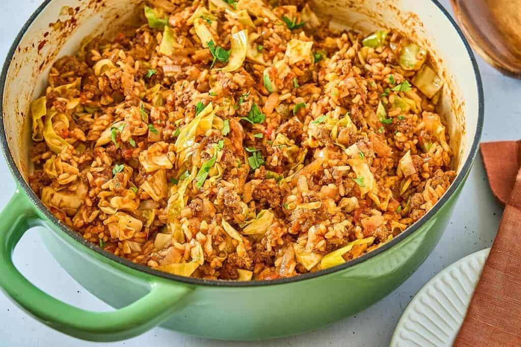 A green Dutch oven filled with cooked unstuffed cabbage casserole, featuring ground meat, rice, cabbage, and tomato sauce&mdash;a perfect choice for Simple 30 Minute Meals.