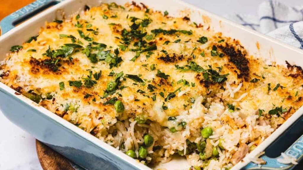 A casserole dish filled with baked rice, vegetables, and melted cheese, topped with chopped herbs and a golden breadcrumb crust.