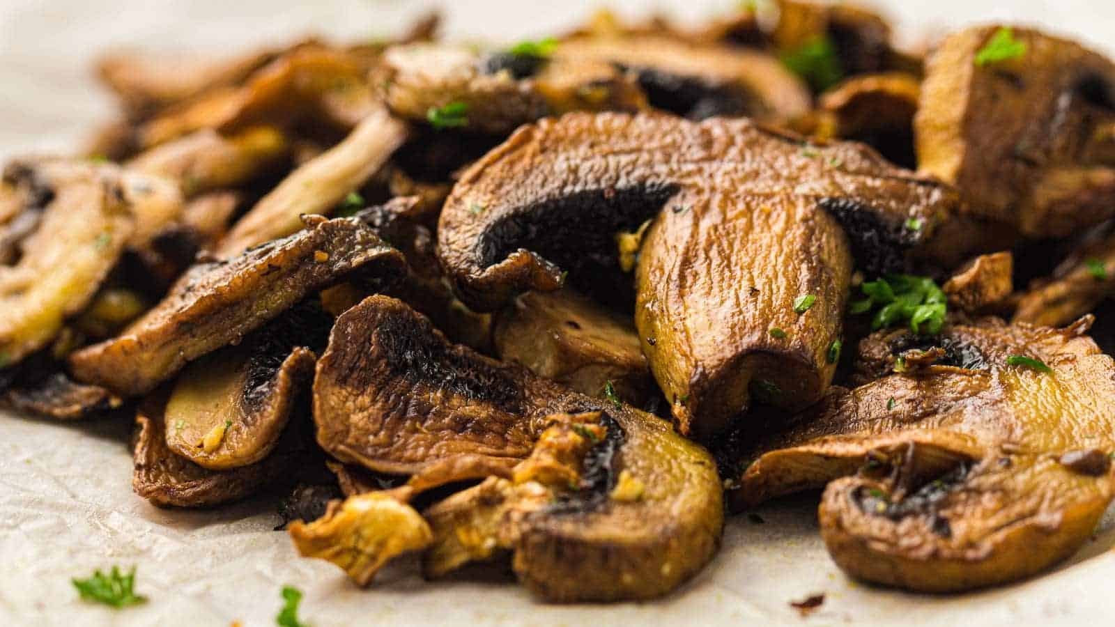 Close-up of sliced, cooked mushrooms garnished with small pieces of fresh herbs on a light-colored surface.