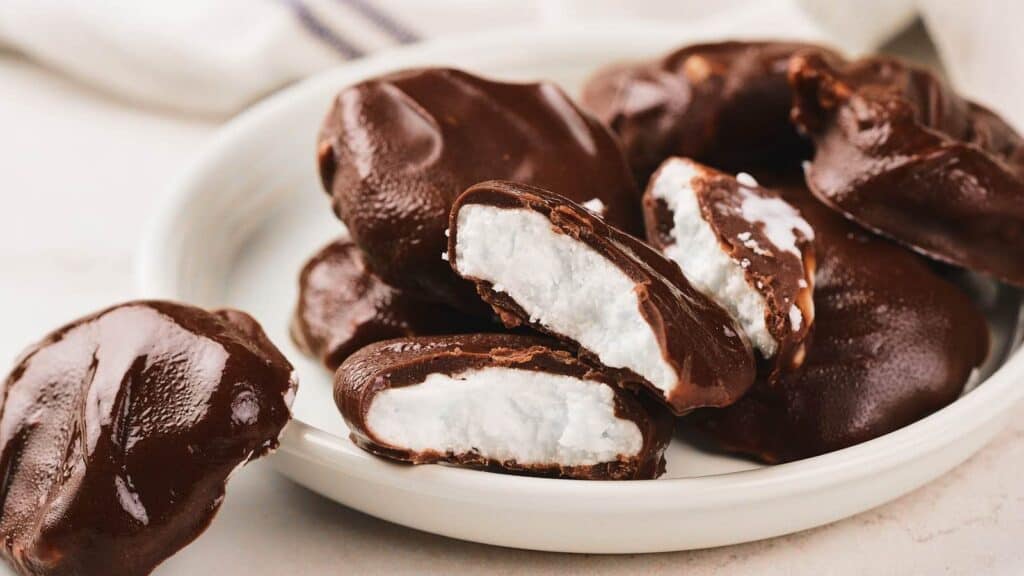 A plate of chocolate-covered peppermint patties, some whole and some cut open to show the white, creamy filling inside.