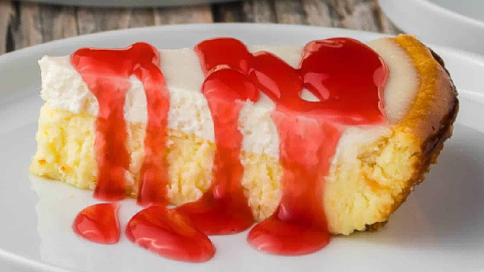 A slice of cheesecake topped with a layer of red strawberry sauce on a white plate.