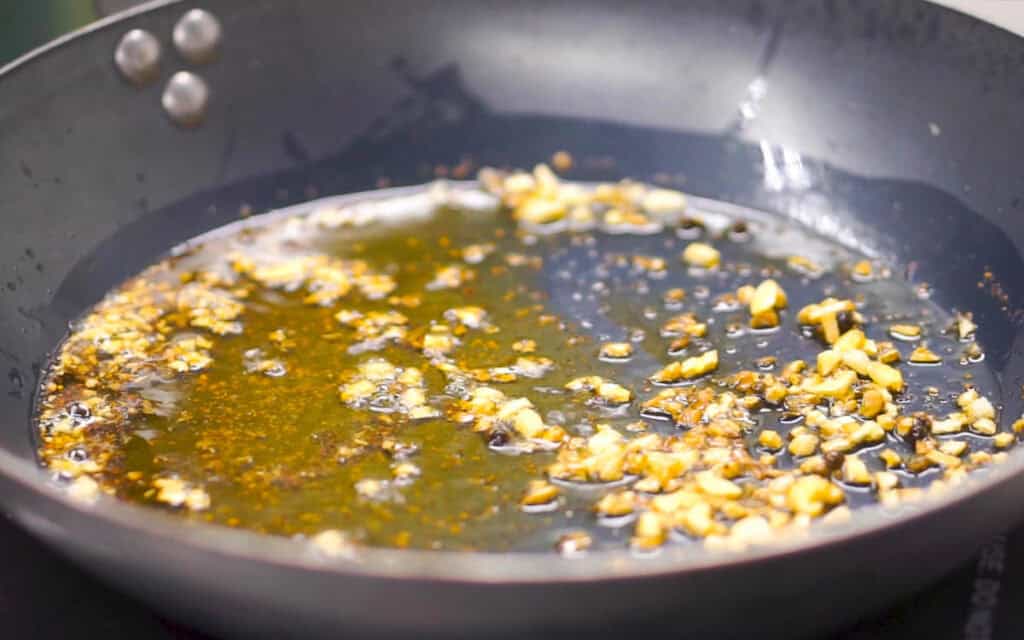 Chopped garlic pieces frying in oil in a black skillet.
